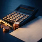 Calculadora, caneta dourada e moedas ao lado de um extrato em branco